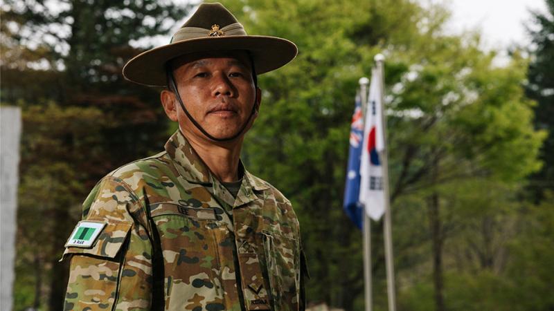 A military man stands outside near an Australian flag and a Republic of Korea flag. 