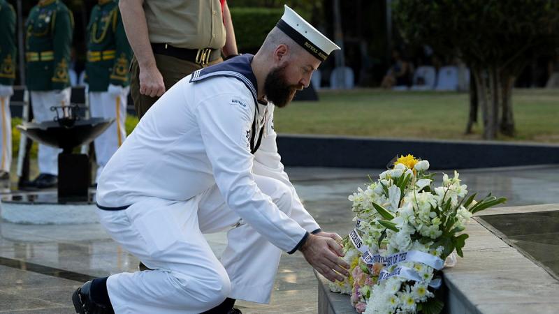An Australian Navy member crouches to lay a wreath of flowers on a step.