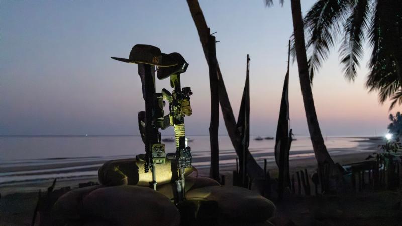 Two guns with hats on top are positioned in sandbags as a memorial during sunrise.