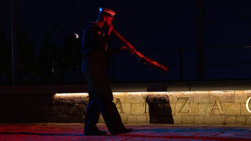 A man in Navy uniform plays a didgeridoo at night, illuminated by red light.