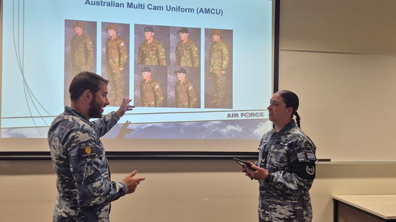 Two military personnel engage in discussion about the content on a PowerPoint display.