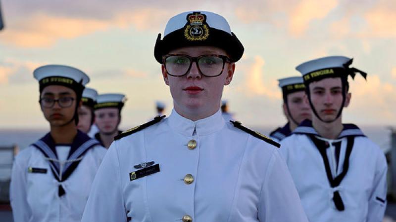 A small group of Navy cadets in whites stand facing the camera.