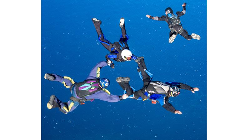 Four people skydive over a large body of water.