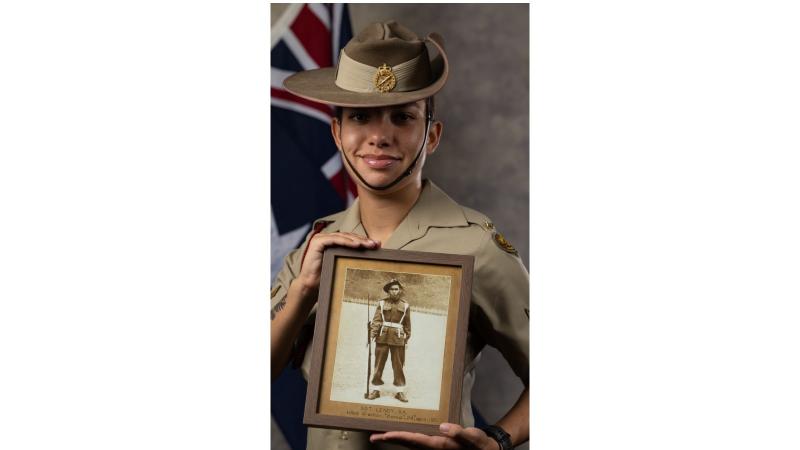 Lance Corporal Imahni Lenoy, dressed in service dress, stands in front of the Australian flag, holding a photo frame with an image of her late Great Uncle, Sergeant Stafford Kenny James 'Len' Lenoy.