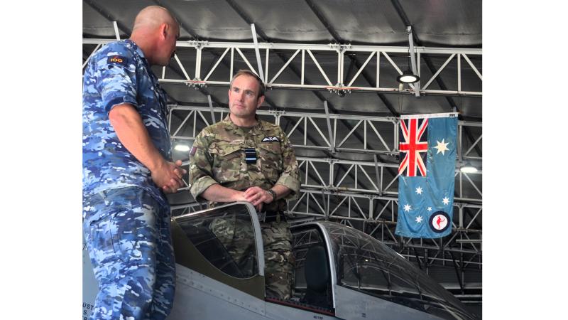Two military men talk while one stands inside the cockpit of an aircraft.