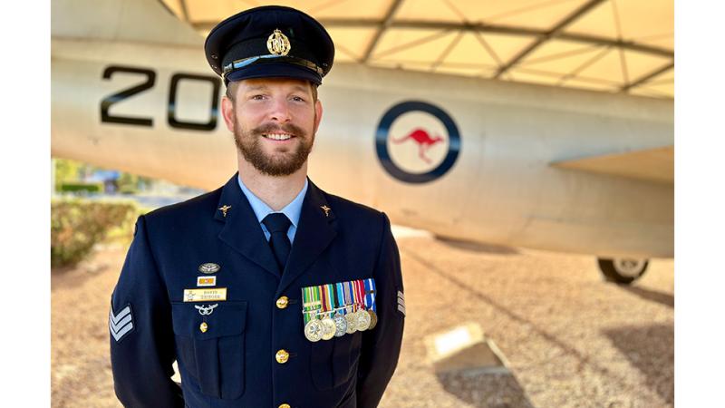 A decorated military member stands before the tail end of an aircraft.
