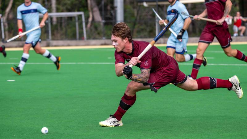 A man taking a swing at the puck during an outdoor hockey game.