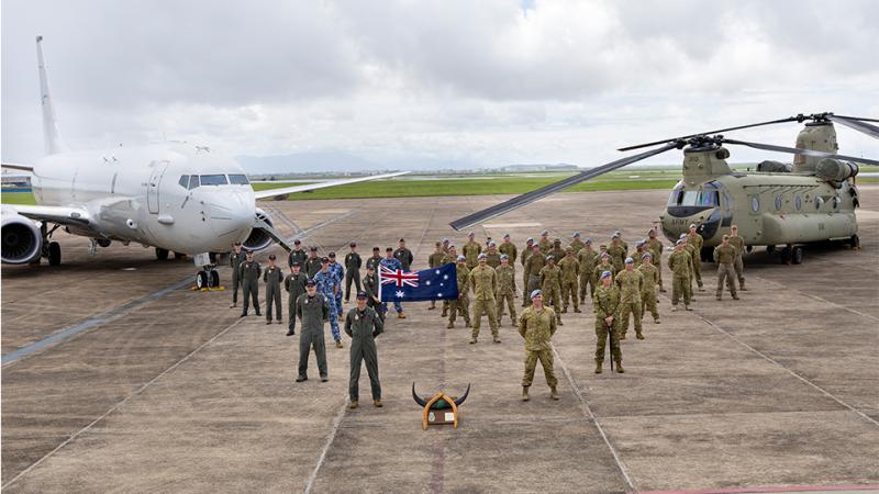 An aircraft, a helicopter, a large group of military personnel and a plaque with animal horns stand in a pyramid formation.