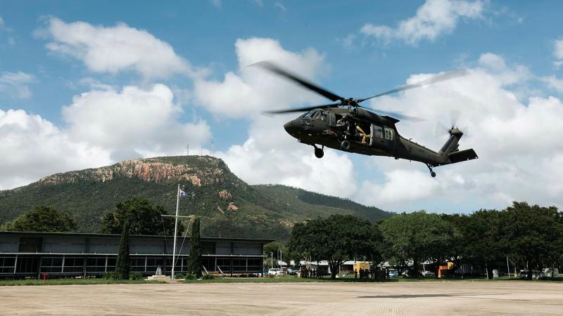 A helicopter with soldiers on board takes off in front of a mountain on a fine day.