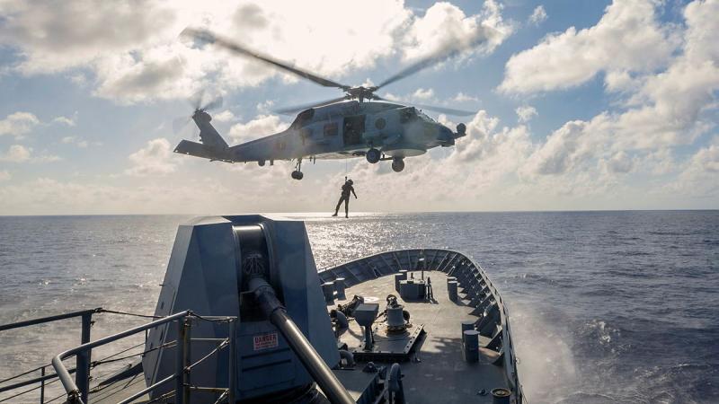 A helicopter hovers above a ship with a person suspended from a line.