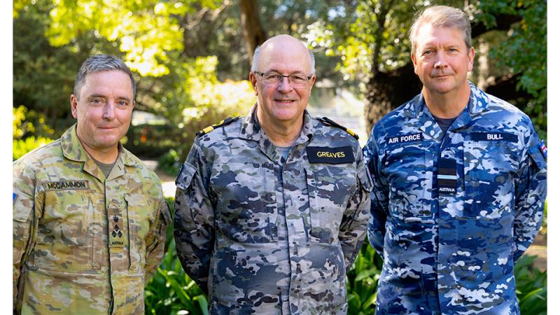 Three military men stand together outside.
