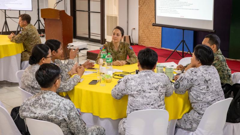 Australian Army Major sits at a table with Philipino armed service personnel.