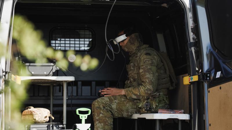 An Australian soldier sits down and controls a drone remotely.