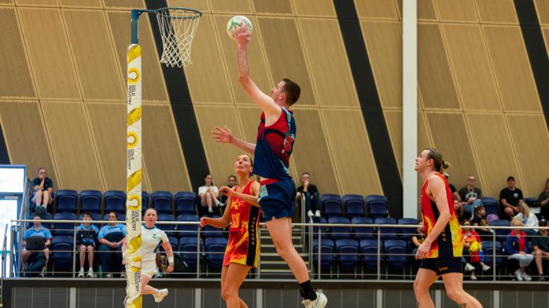 A male netball player takes a jump shot at goal.