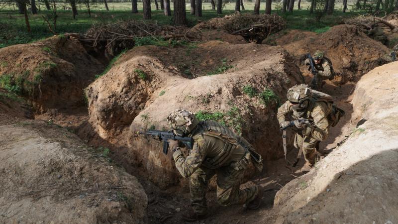 Army personnel move their way through a trench with guns.