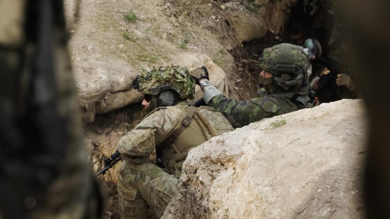 A close up shot of an Australian and Finnish soldier beside one another demonstrating a trench clearance.