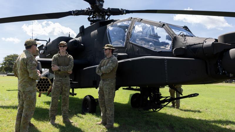 Four men in uniform stand beside a military helicopter and talk outdoors.