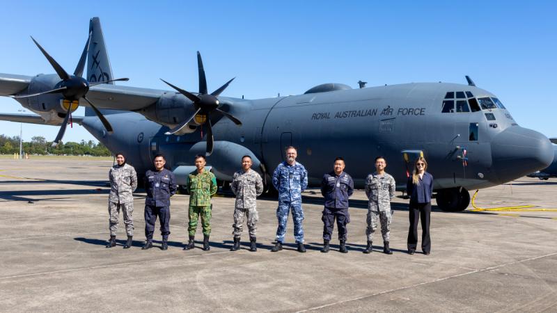 A group of military personnel stand in a row on the tarmac in front of an aircraft.