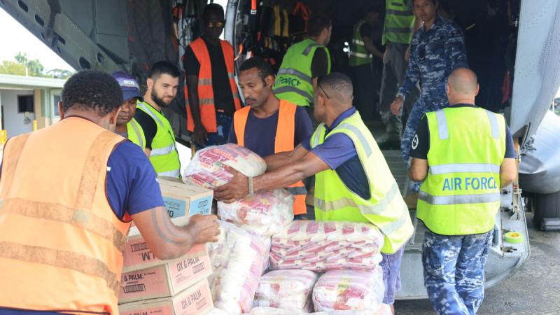 A group of military personnel wearing hi-vis vests load boxes into a aircraft.