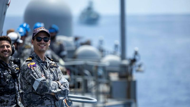 Navy personnel stand on a ship deck at sea.