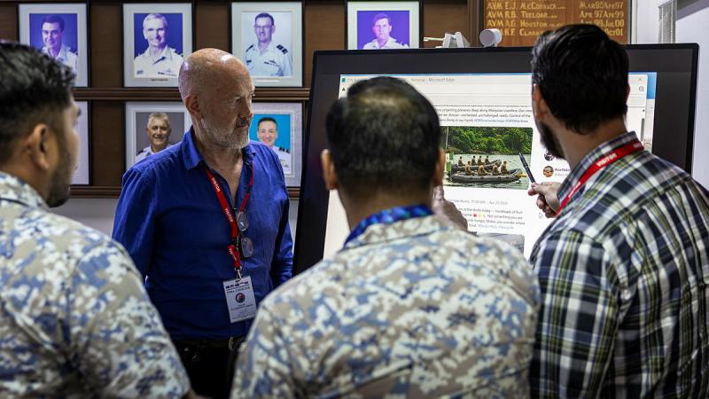 A man faces three others as he explains a display on a board.