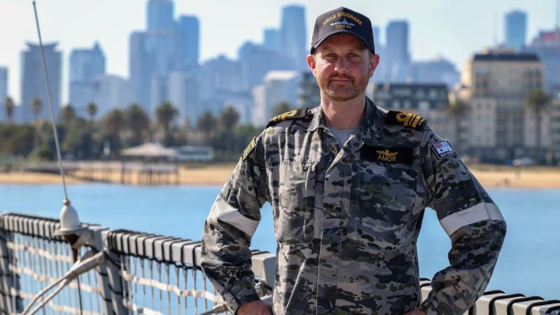 Navy commander stands on deck hands on hips facing the camera.