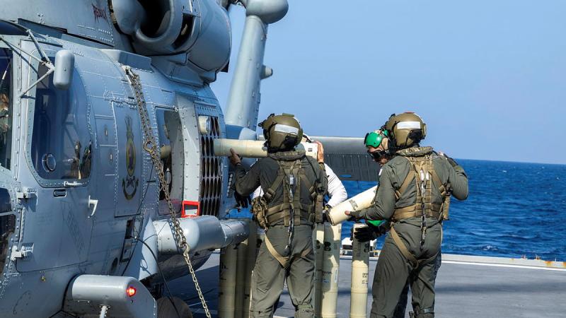 Defence personnel load large cylindrical objects into the side of a helicopter.