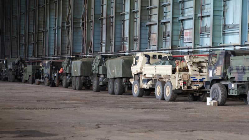 Army trucks lined up at an industrial site.