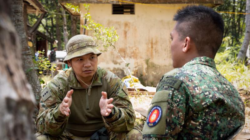 Australian Army Captain Jeffrey Correa makes hand gestures as he sits with a member of the Armed Forces of the Philippines in the jungle having a discussion.