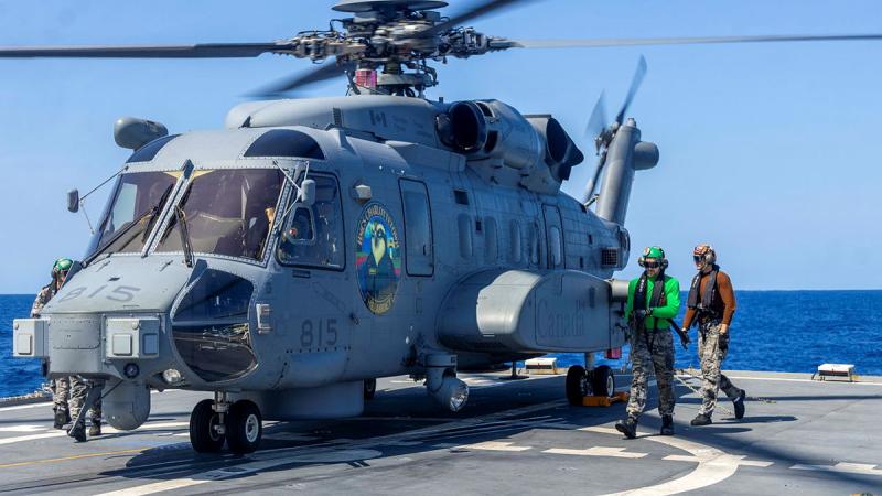 Two people walk near a helicopter on the flight deck of a ship.
