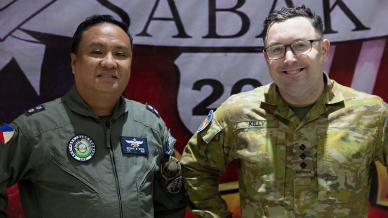Two men in military uniform stand side by side indoors.