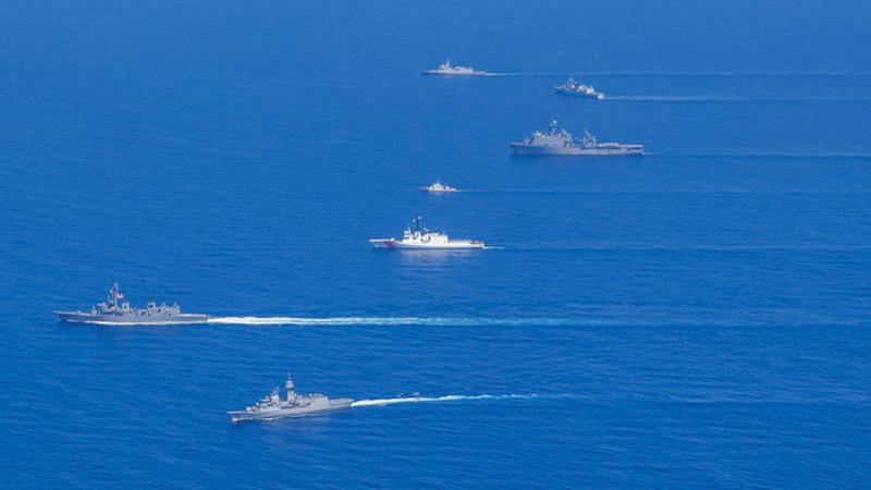 Seven ships sail in the same direction in a deep blue sea.