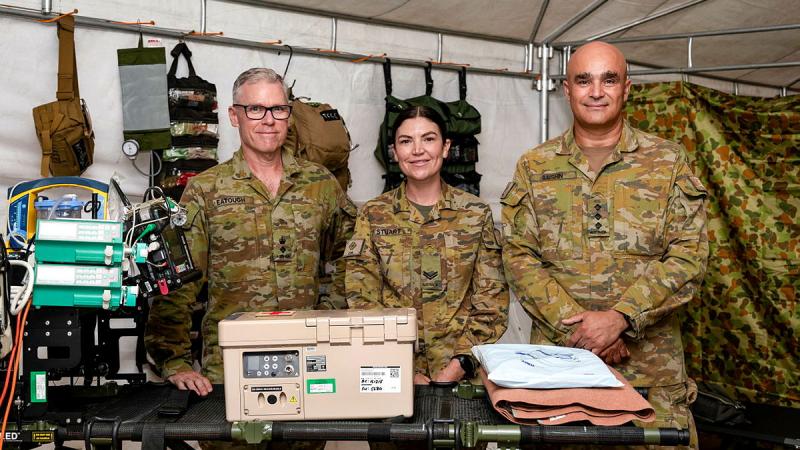 Three Army members, surrounded by medical equipment, stand in a canvas tent.