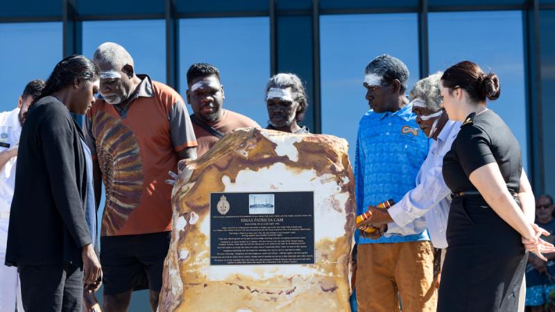 A group of Indigenous people gather around a memorial stone. 