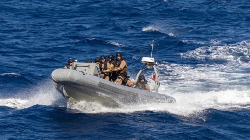 People in brown uniforms travelling on a rigid-hull inflatable boat through a wavy sea.
