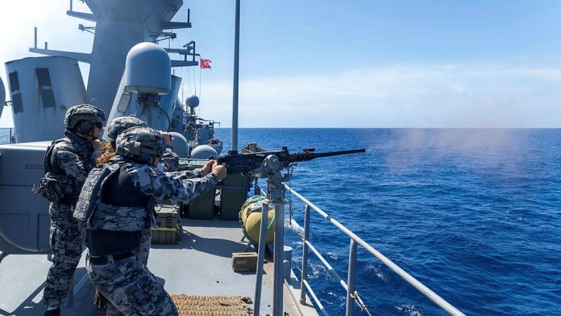 Navy personnel fires guns out to sea off the side of a ship.