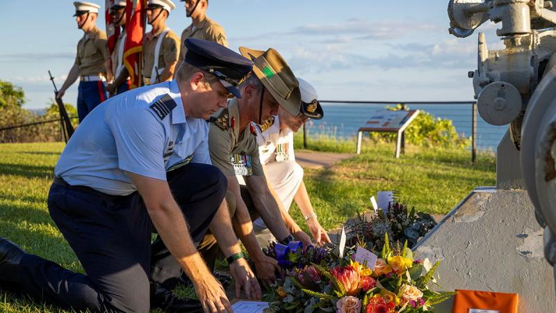 Three Australian Defence Force members, one each from Navy, Army and Air Force, kneel to place flower wreaths on the ground.