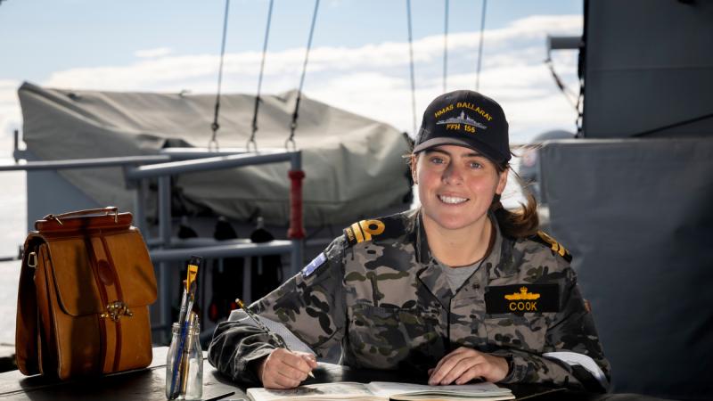 A Navy officer paints with watercolours on the deck of a ship.