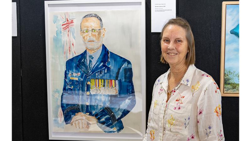 A woman stands before a watercolour artwork of a decorated military man.