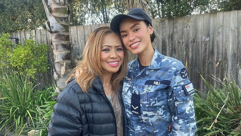 A young woman in RAAF uniform stands with her mother in front of a fence and greenery.