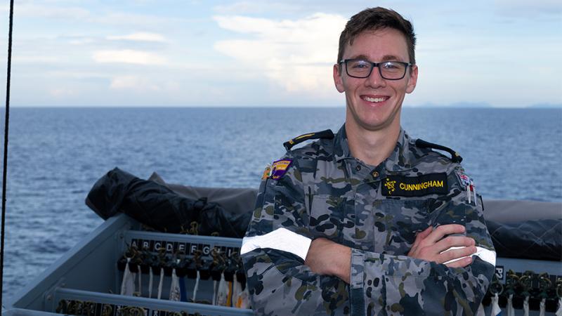 A military man stands on a boat out at sea.