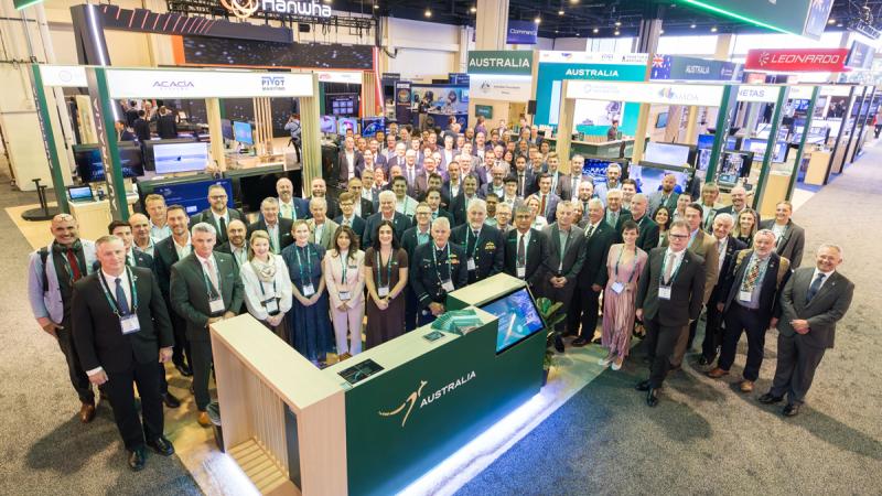 A large group of people gather for a photo in a conference exhibition hall.