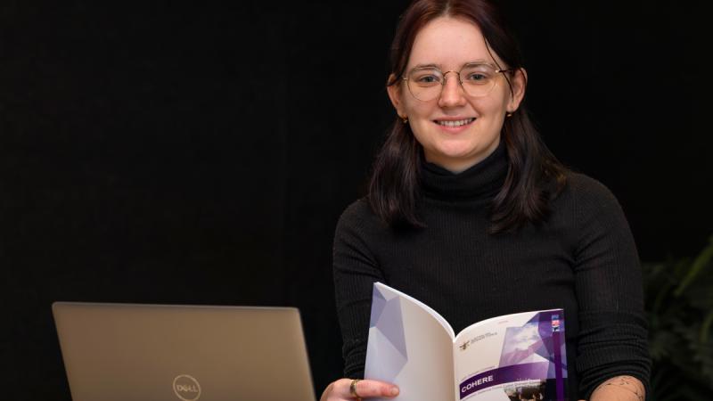 Sophie Zardins sits in front of a laptop holding the COHERE cyber domain publication.