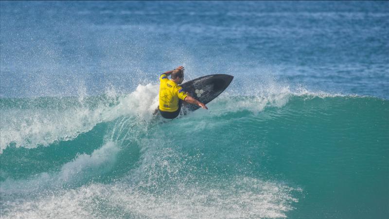 A man in a yellow rash shirt surfing the peak of a wave.