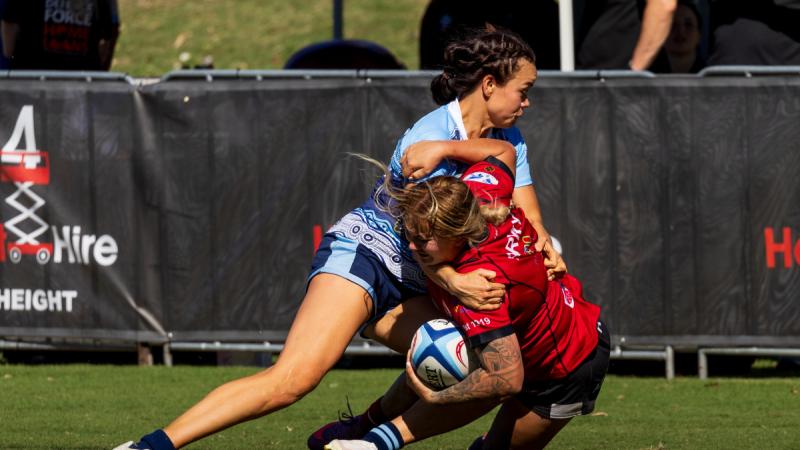 Two female rugby players tackling for the ball during a game.
