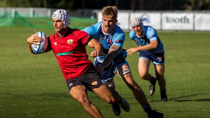 Three men in rugby uniforms play and try to tackle the ball.