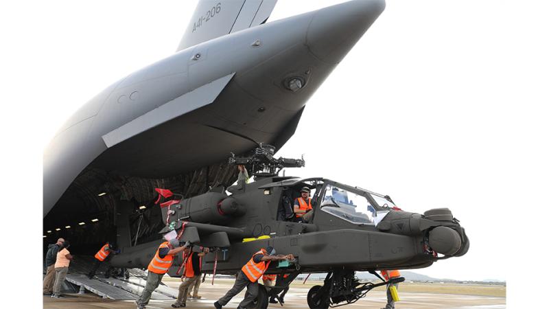 People in high-visibility vests pushing a helicopter out of an aircraft’s cargo hatch onto the tarmac, with one person sitting in the cockpit.