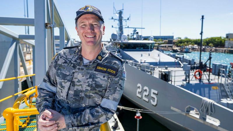 A sailor stands smiling in front of a ship