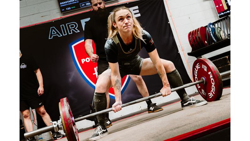 A woman in athleisure attempts to lift a weighted barbell.