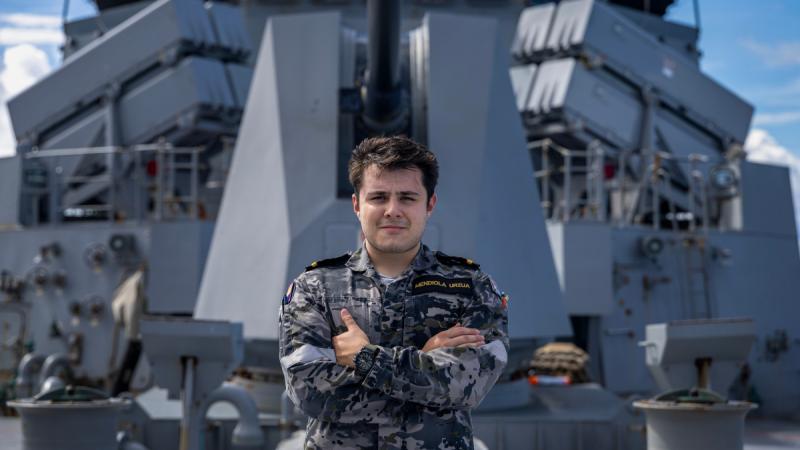 A Navy Officer stands with arms crossed on the deck of HMAS Toowoomba